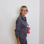 Woman in gray outfit holding a pink bag against a white wall