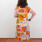 Woman wearing a colorful patchwork dress against a white wall.