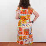Woman wearing a colorful patchwork dress against a white wall.