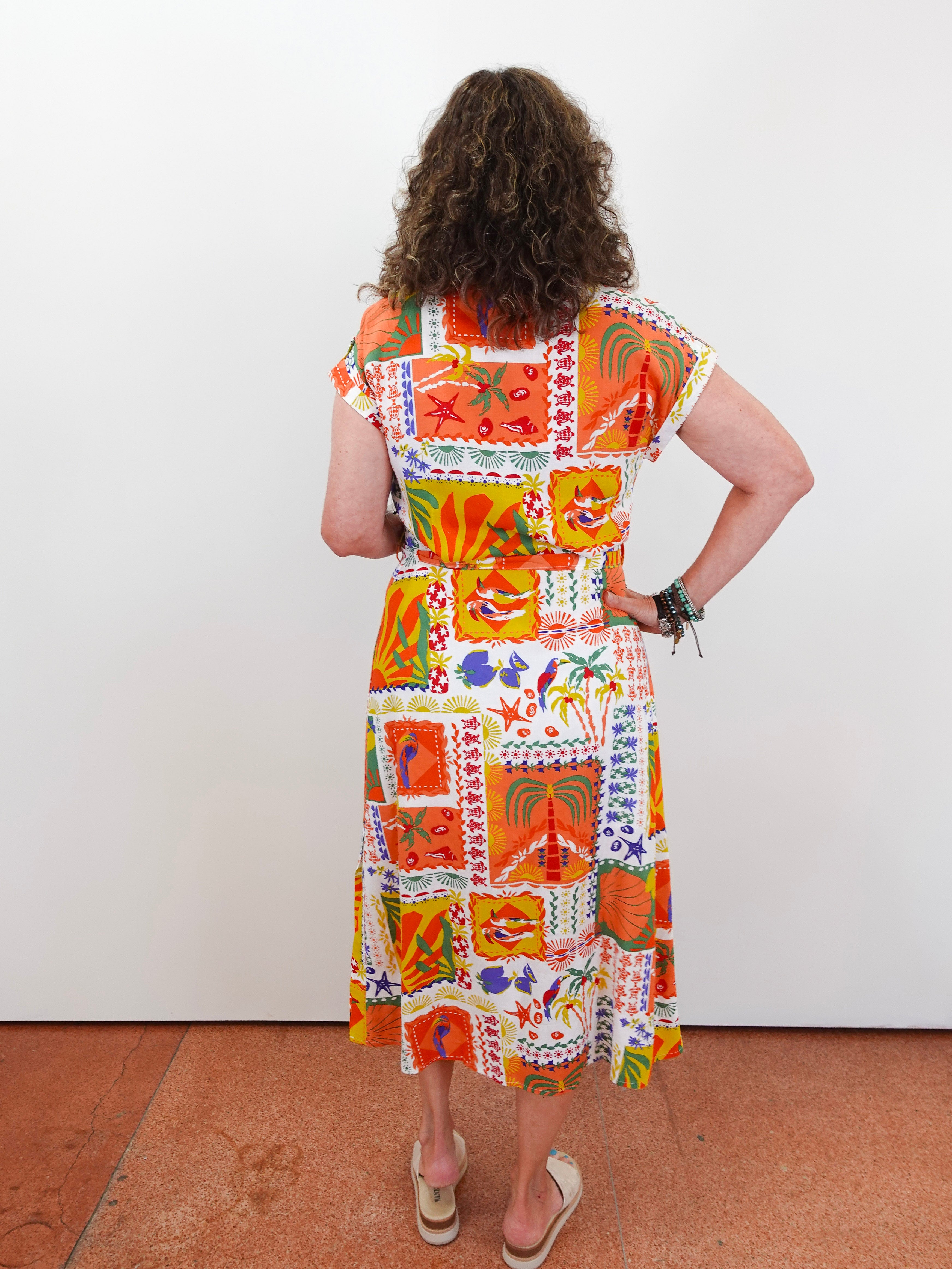 Woman wearing a colorful patchwork dress against a white wall.