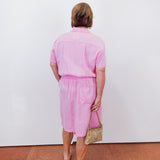 Person wearing a pink outfit standing against a white wall.