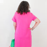 Person wearing a bright pink dress with a green bag on a plain background