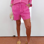 Person wearing a pink outfit with shorts and a top, standing against a white wall.