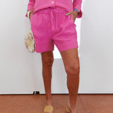 Person wearing a pink outfit with shorts and a top, standing against a white wall.
