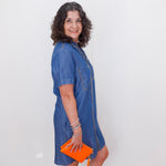 Woman wearing a blue dress holding an orange clutch against a white background