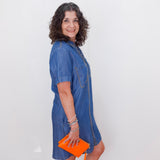 Woman wearing a blue dress holding an orange clutch against a white background