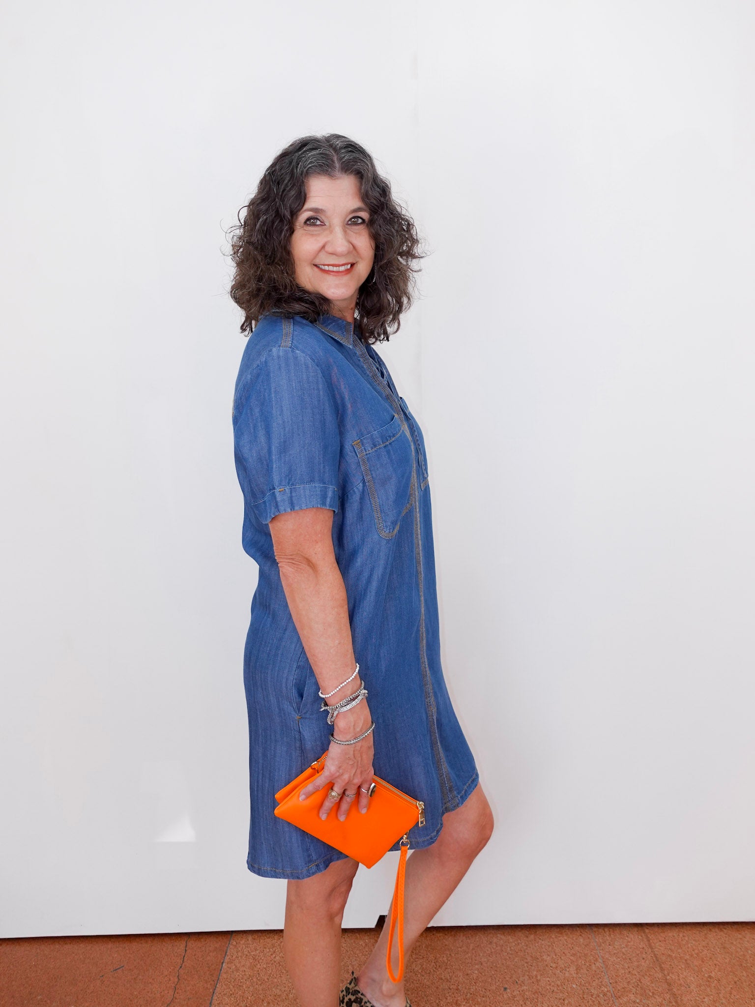 Woman wearing a blue dress holding an orange clutch against a white background
