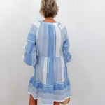 Woman wearing a blue and white striped dress against a white wall.