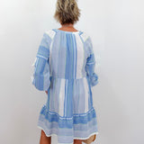 Woman wearing a blue and white striped dress against a white wall.