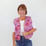 Woman wearing a colorful quilted vest over a white shirt with blue jeans on a white background