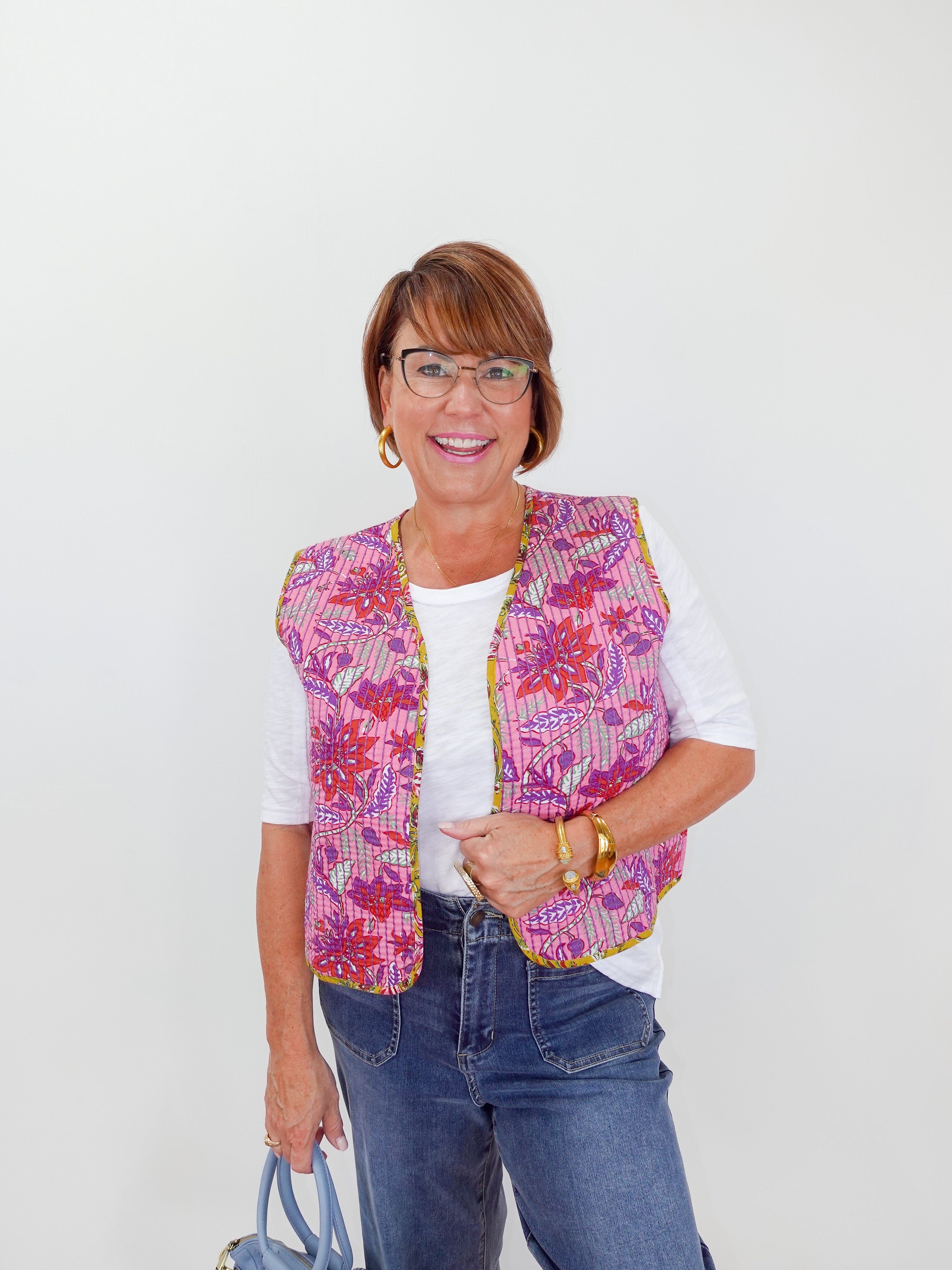 Woman wearing a colorful quilted vest over a white shirt with blue jeans on a white background