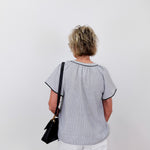 Person wearing a light gray blouse with black trim on a white background