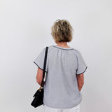 Person wearing a light gray blouse with black trim on a white background