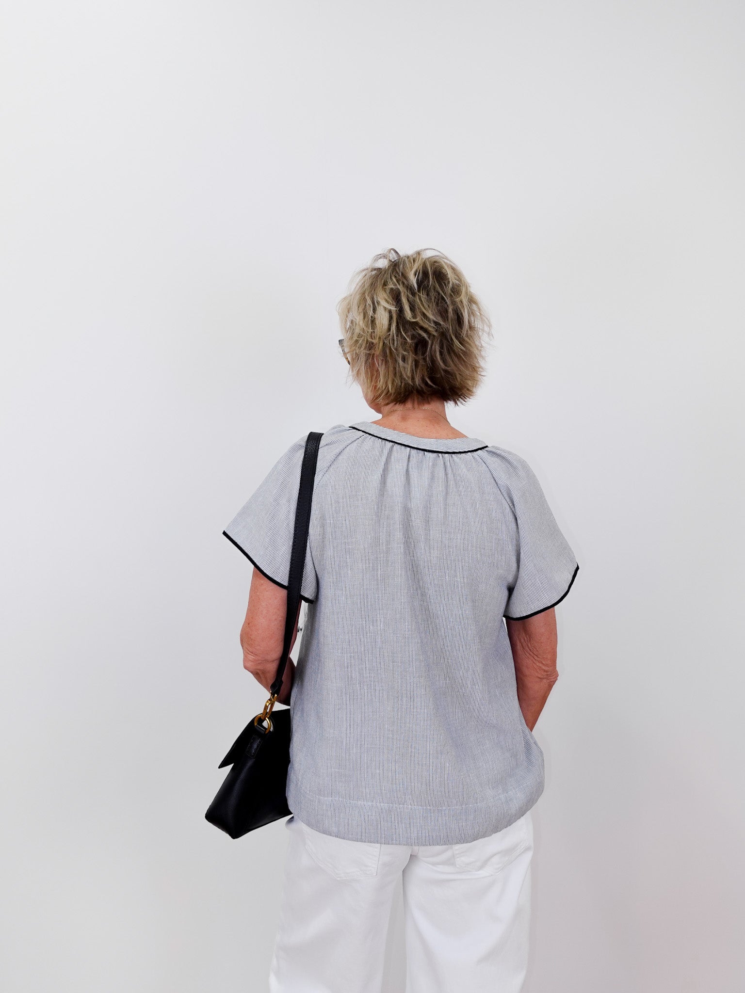 Person wearing a light gray blouse with black trim on a white background