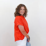 Woman wearing an orange shirt and white pants against a plain background