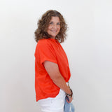 Woman wearing an orange shirt and white pants against a plain background