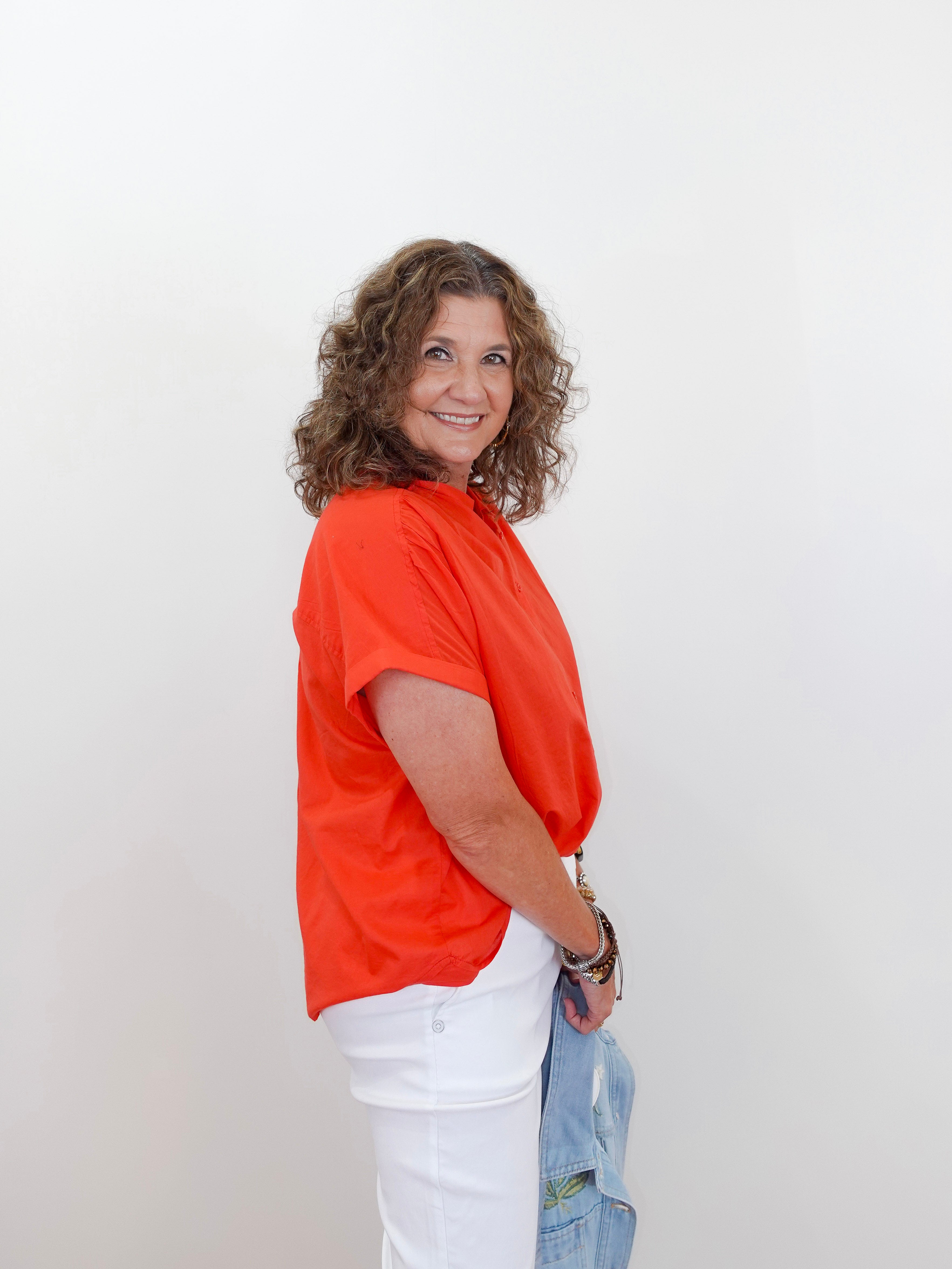 Woman wearing an orange shirt and white pants against a plain background