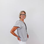 Woman wearing a gray short-sleeve shirt with a black trim against a white background