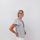 Woman wearing a gray short-sleeve shirt with a black trim against a white background