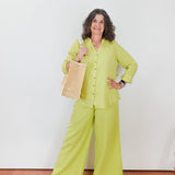 Woman in a bright green outfit holding a woven bag against a white wall.