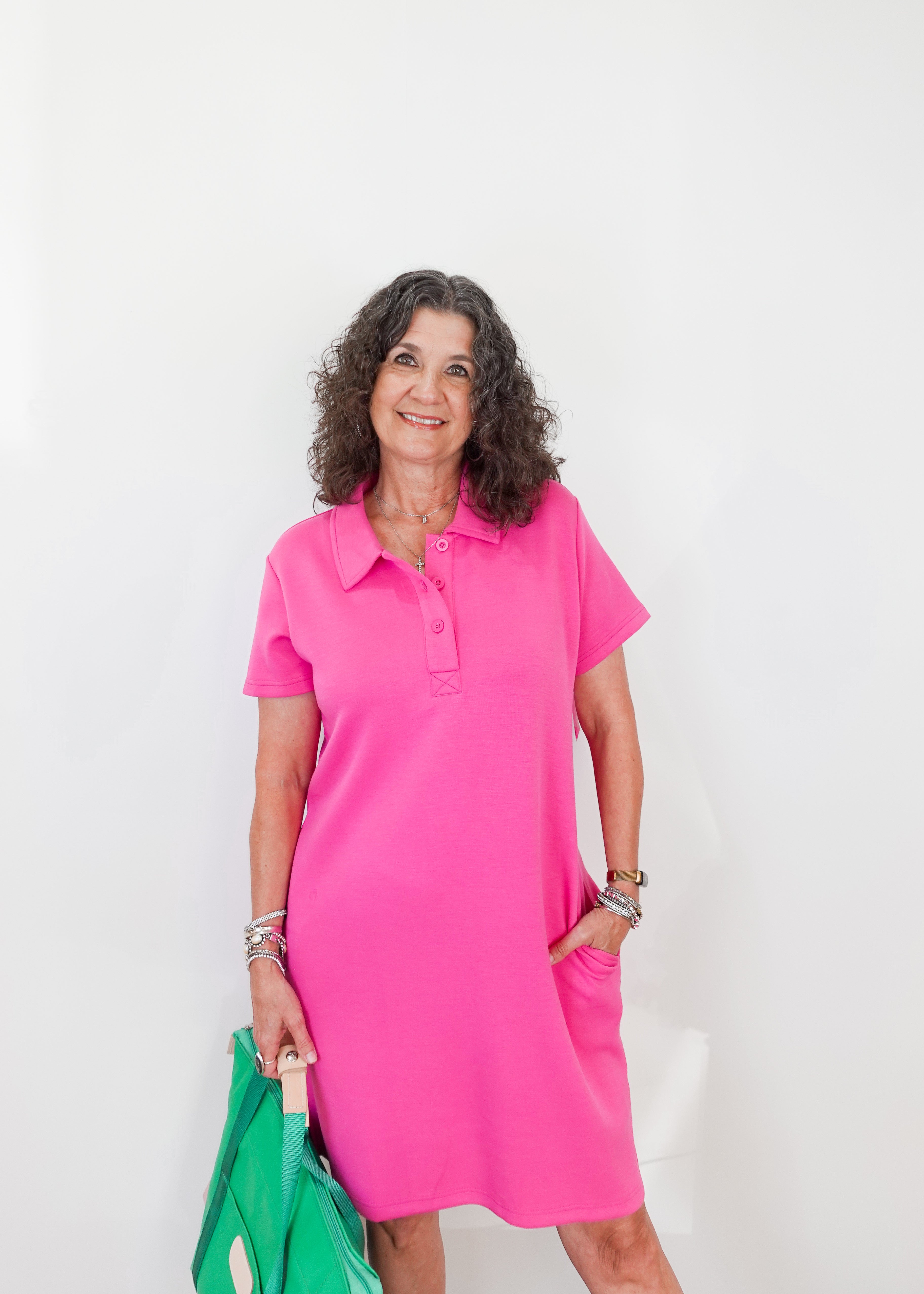 Woman wearing a pink dress holding a green bag against a white background