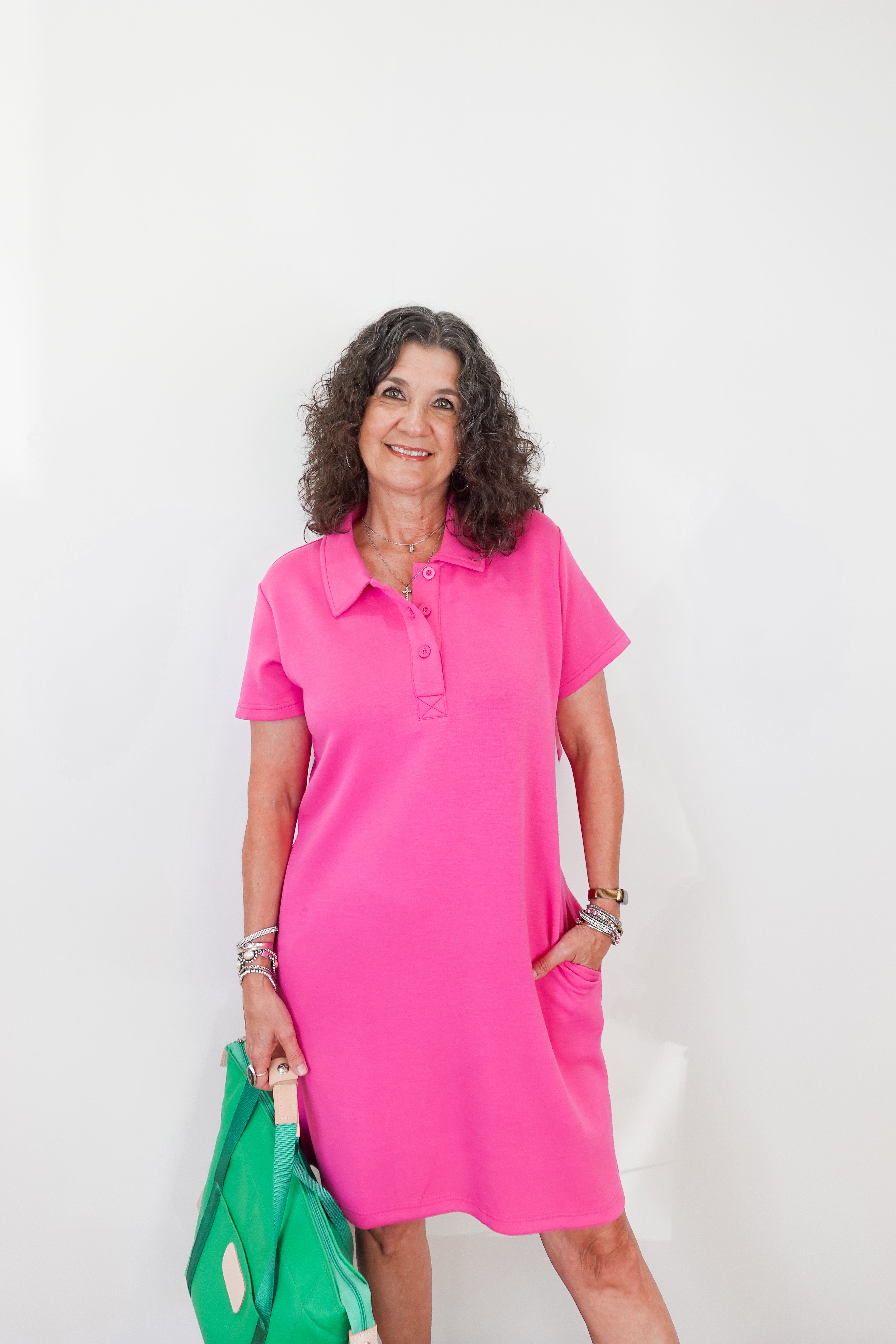 Woman wearing a pink dress holding a green bag against a white background