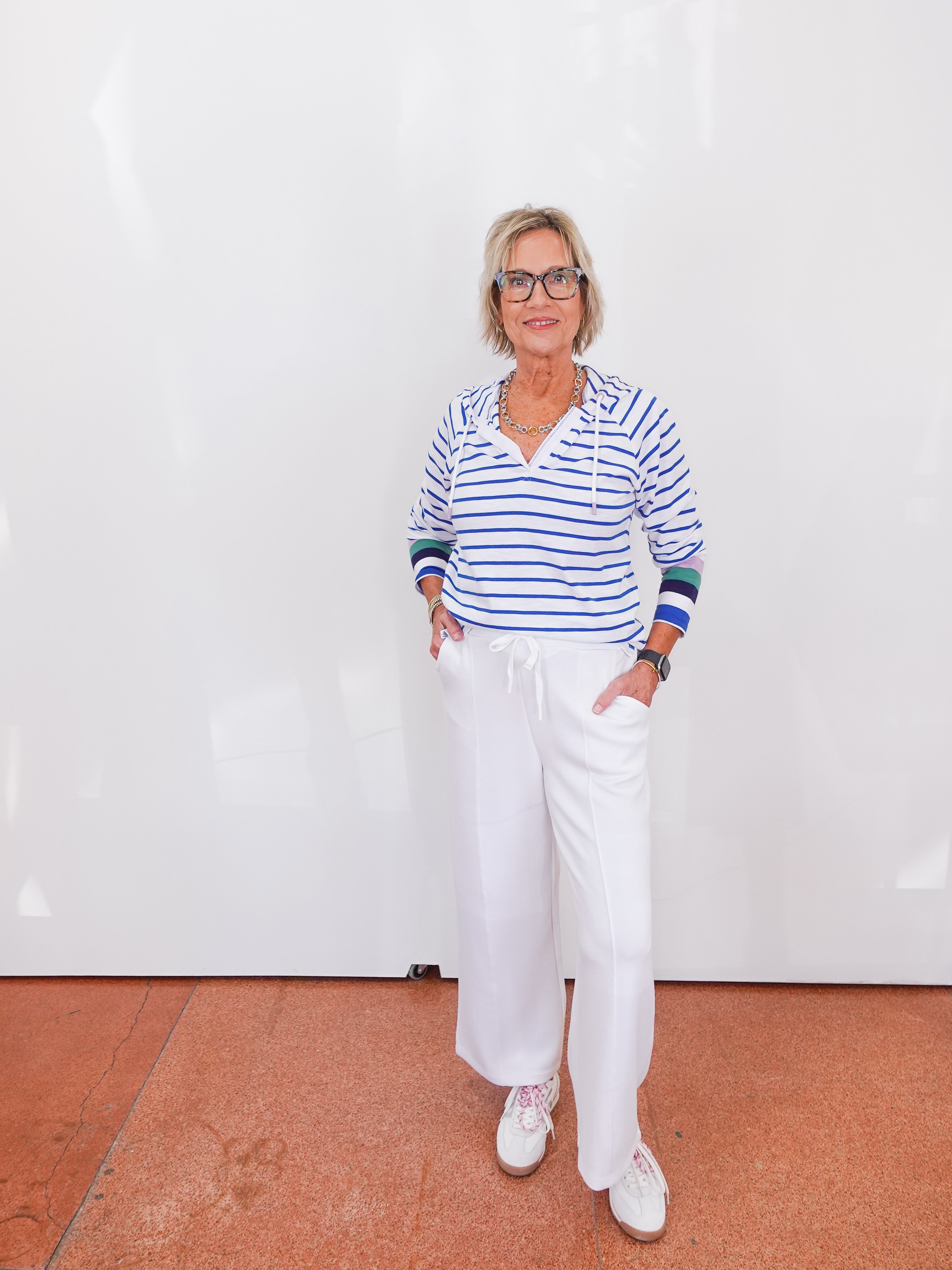 Person wearing a striped shirt and white pants standing on a red floor with a white wall background