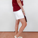 Person wearing a red shirt, white shorts, and white shoes on a plain background