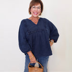 Woman wearing a blue top and jeans, holding a tan handbag against a white background