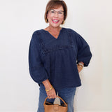 Woman wearing a blue top and jeans, holding a tan handbag against a white background