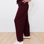Person wearing burgundy pants and white sneakers on a light wooden floor.