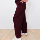 Person wearing burgundy pants and white sneakers on a light wooden floor.