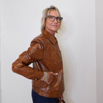 Person wearing a brown leather jacket against a white wall