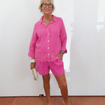 Woman wearing a pink outfit standing against a white wall.