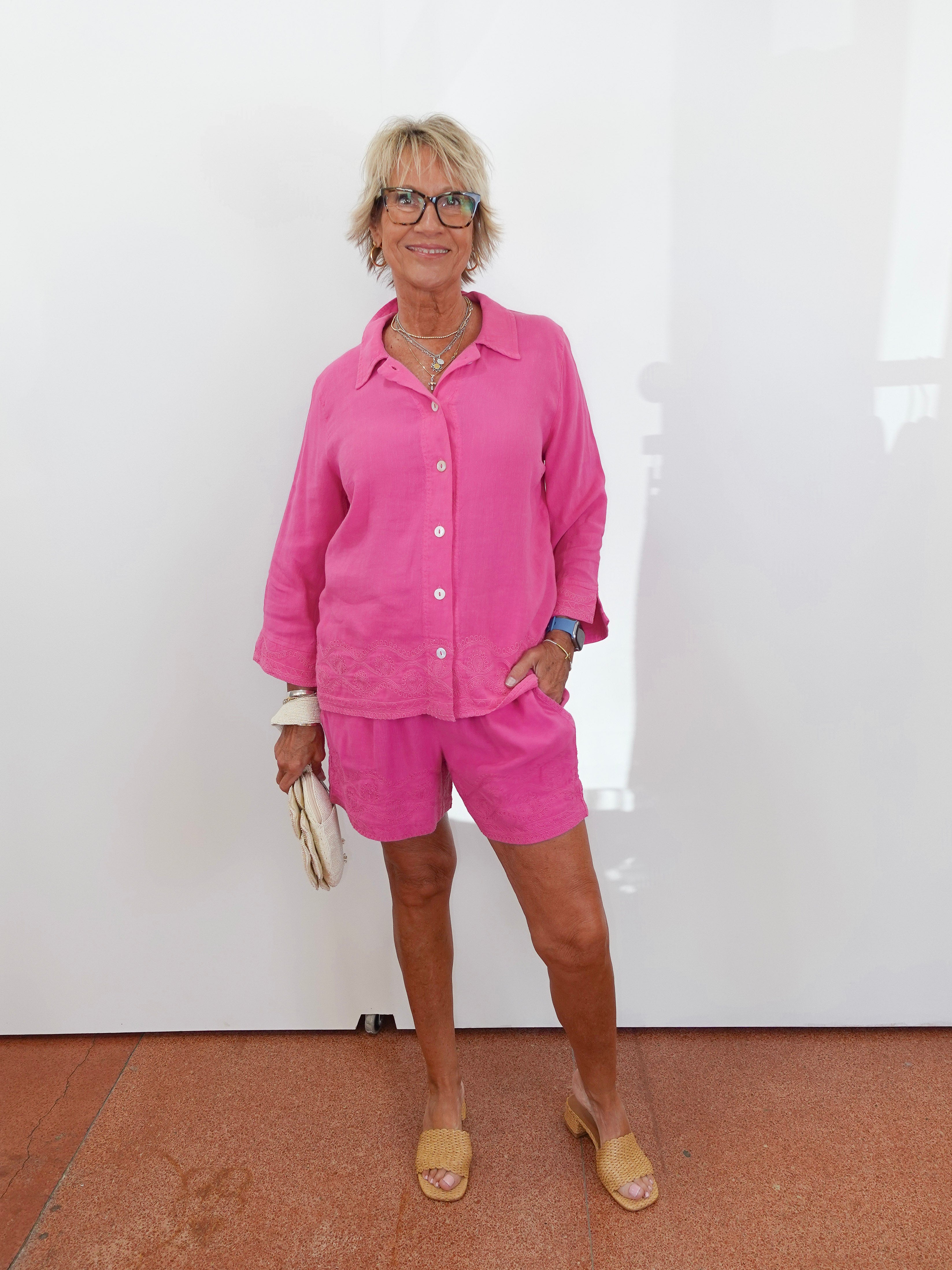Woman wearing a pink outfit standing against a white wall.