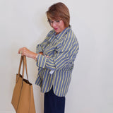 Woman in a striped shirt holding a tan handbag against a white wall