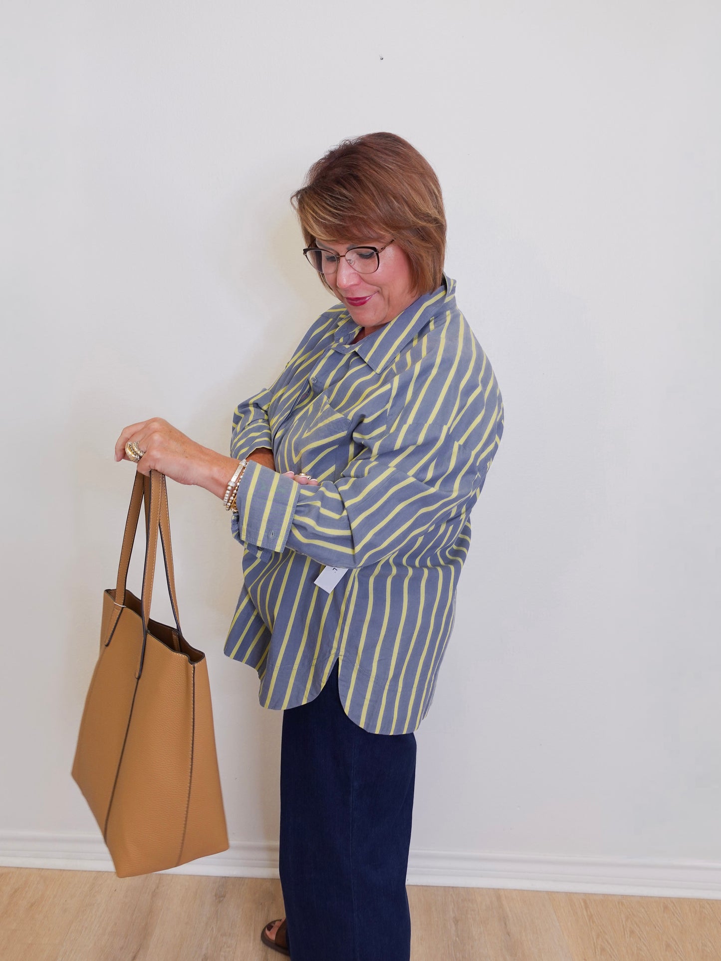 Woman in a striped shirt holding a tan handbag against a white wall