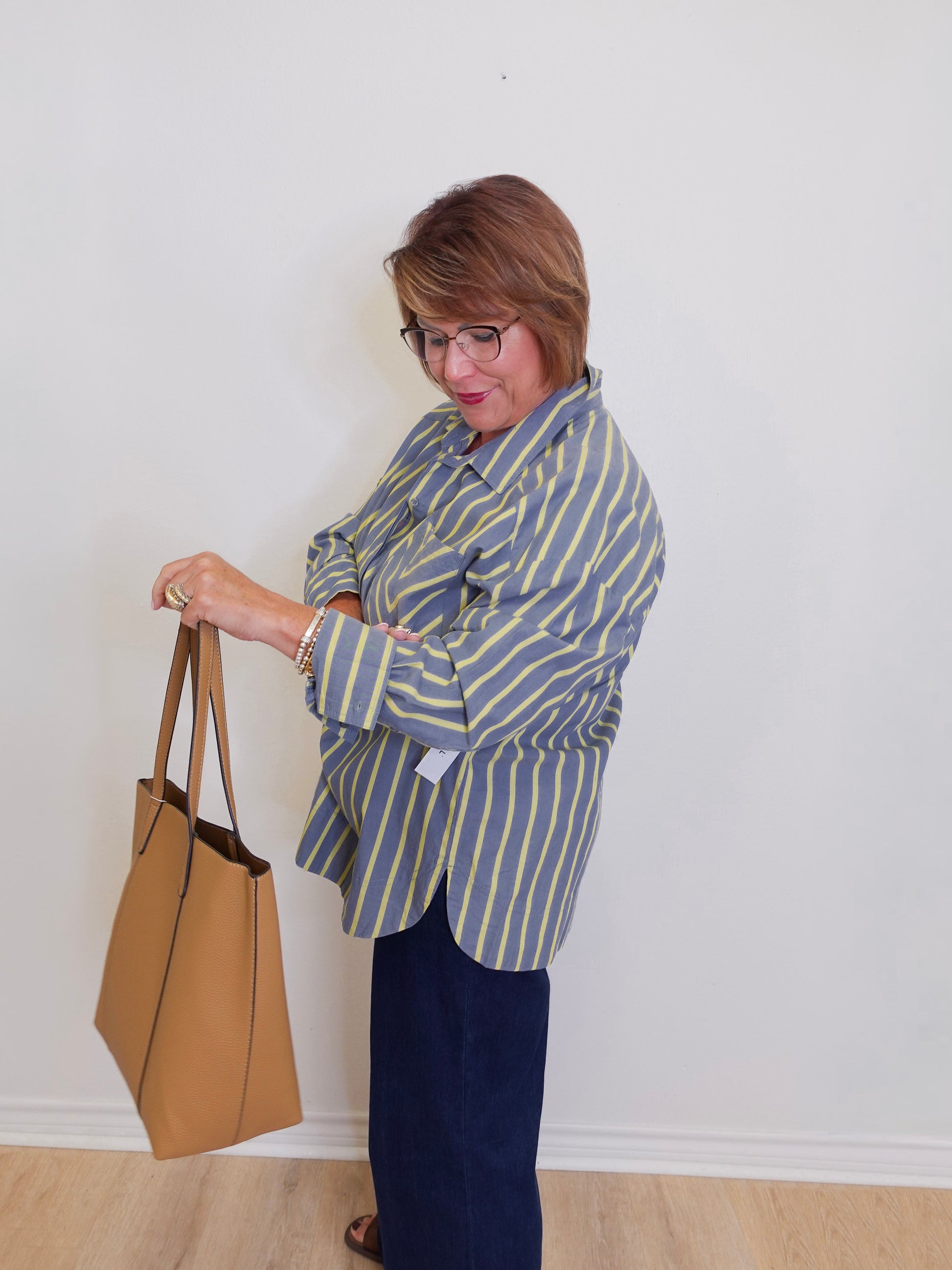 Woman in a striped shirt holding a tan handbag against a white wall