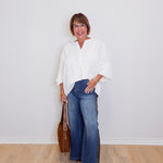 Woman wearing a white blouse, blue jeans, and brown shoes against a plain white background.