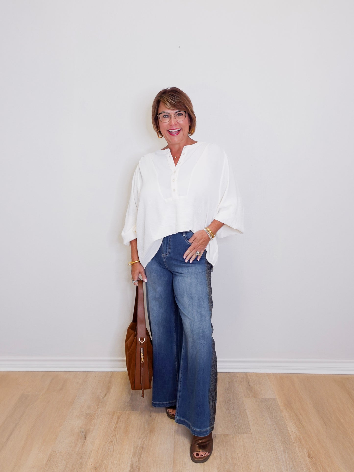 Woman wearing a white blouse, blue jeans, and brown shoes against a plain white background.