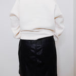 Person wearing a white sweater and black leather skirt against a plain background