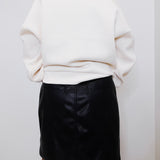 Person wearing a white sweater and black leather skirt against a plain background