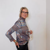 Woman wearing a patterned shirt and glasses against a white wall