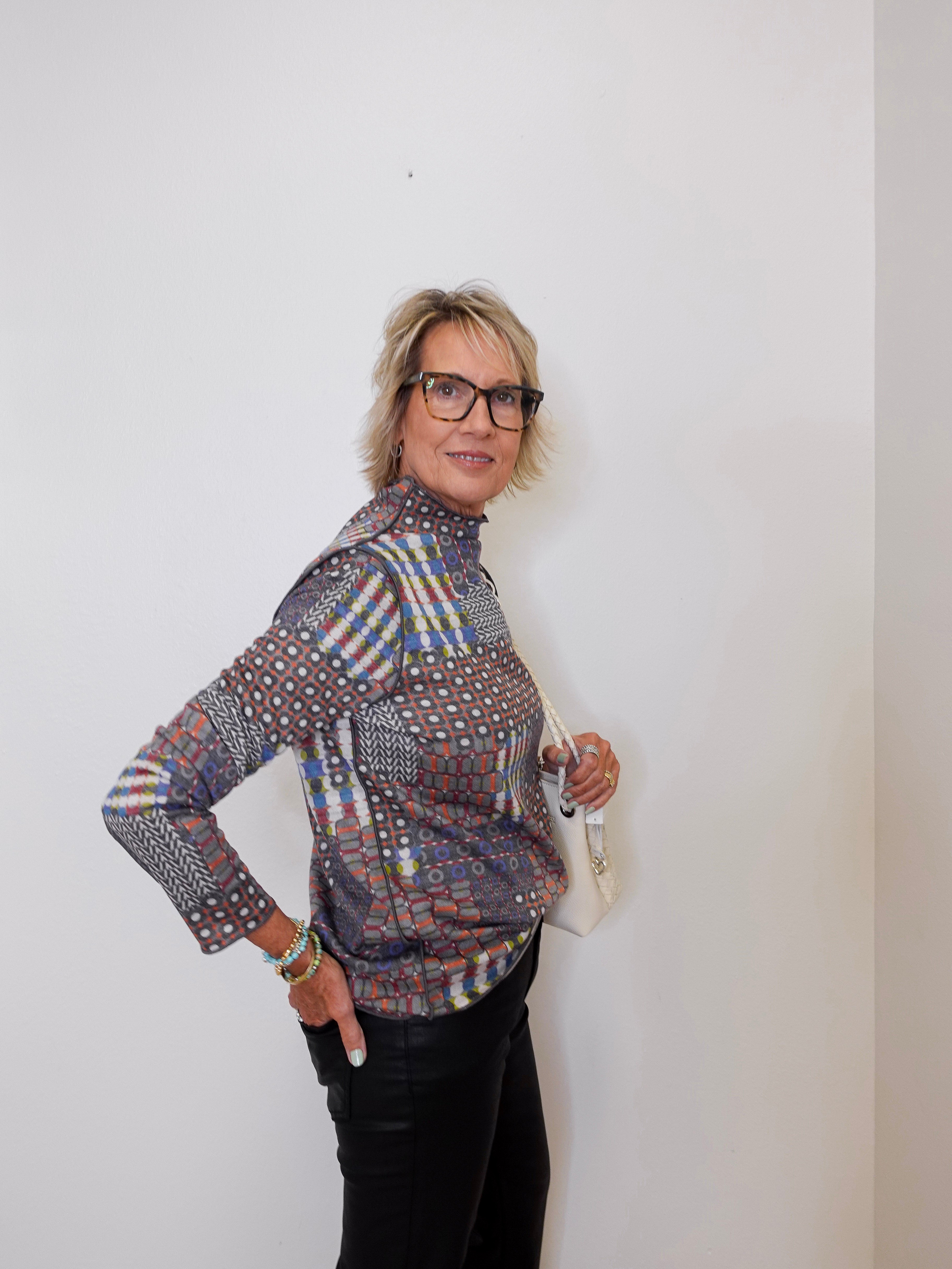 Woman wearing a patterned shirt and glasses against a white wall