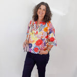 Woman wearing a colorful floral blouse and navy pants against a white background