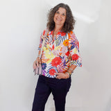 Woman wearing a colorful floral blouse and navy pants against a white background