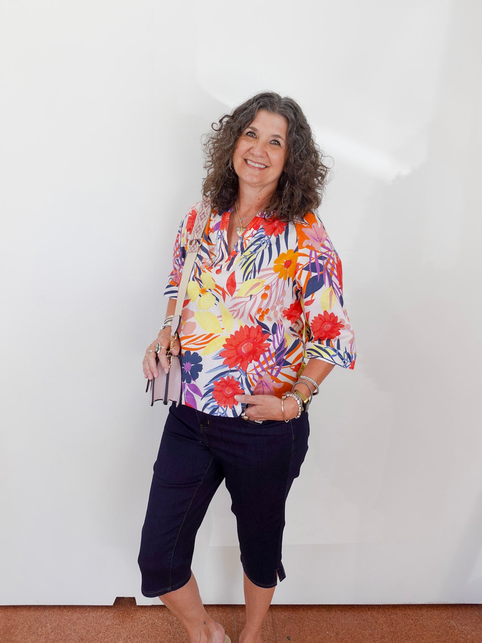 Woman wearing a colorful floral blouse and navy pants against a white background