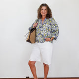 Woman wearing a floral blouse and white shorts, holding a bag against a white background