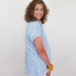 Woman wearing a light blue blouse with white patterns against a plain background