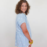 Woman wearing a light blue blouse with white patterns against a plain background